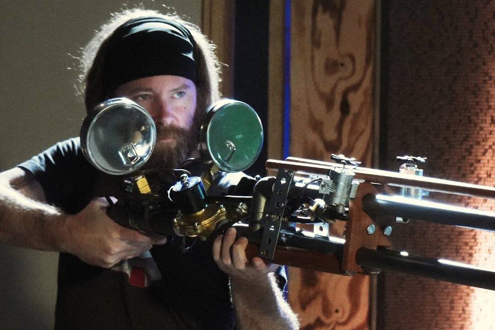 Man wearing headband is holding a large steampunk firearm